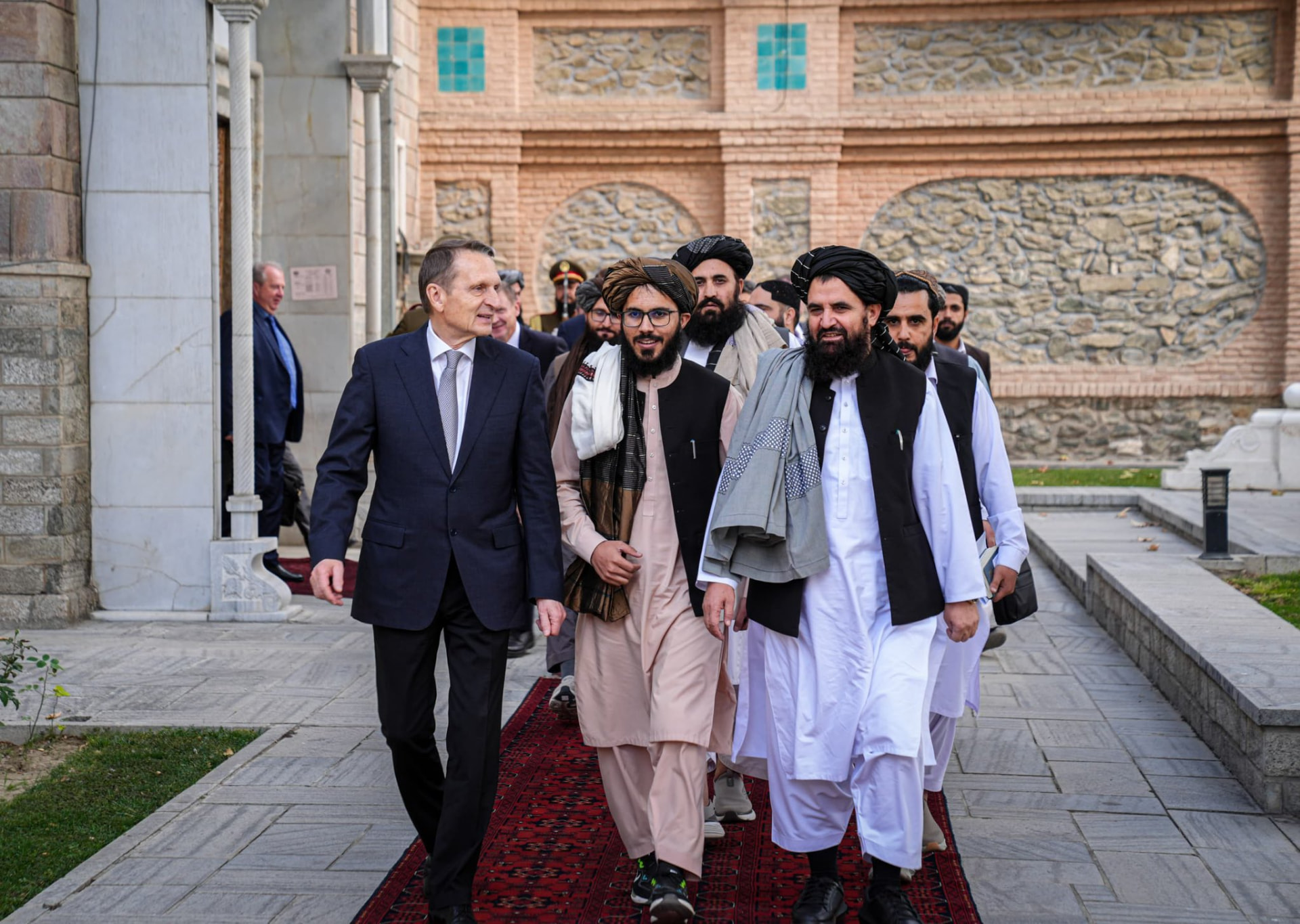 Russian official walking with Taliban representatives in a courtyard